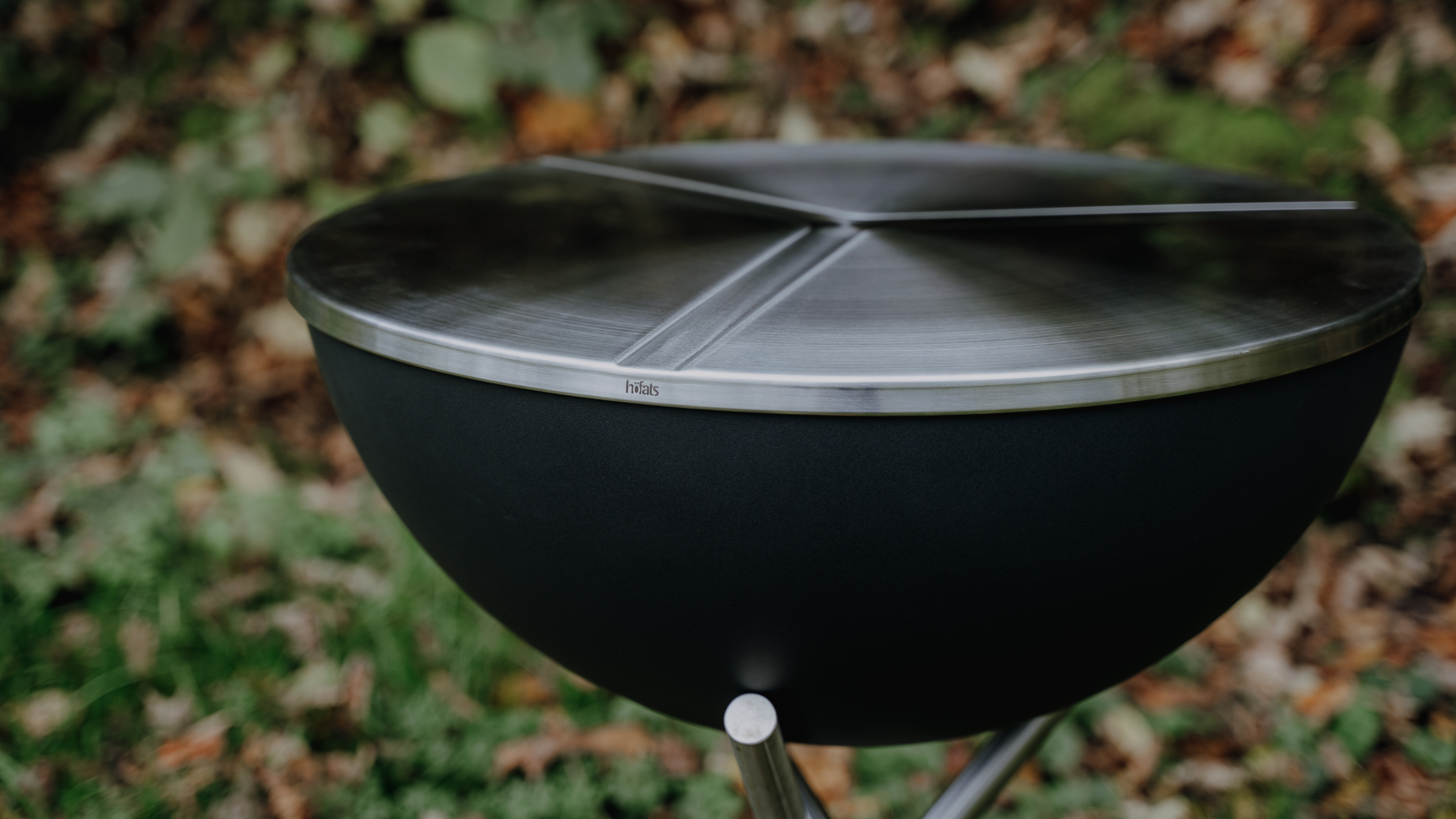 A depiction of a black grill sitting on top of a green field, featuring the 00478 Bowl 57 Lid with starstand as a central and purposeful element.