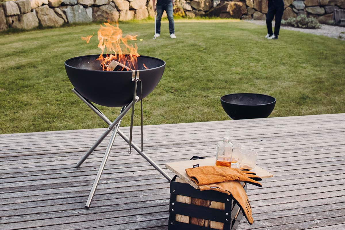 A fire pit with a fire in it, with the 00342 Bowl 57 Tripod adding a functional and elegant touch to the scene.