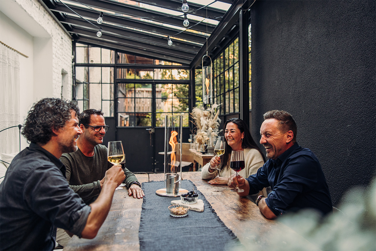 Three men sitting at a table with wine glasses, with the 00695 Spin 1200 Tablefire silver adding a functional and elegant touch to the scene.