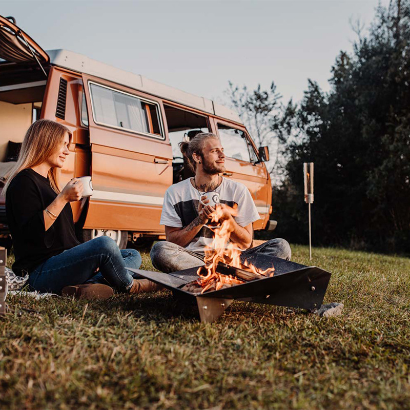 An inviting scene with a couple sitting on the grass next to a camper van, highlighted by the presence of the Triple Fireplace
