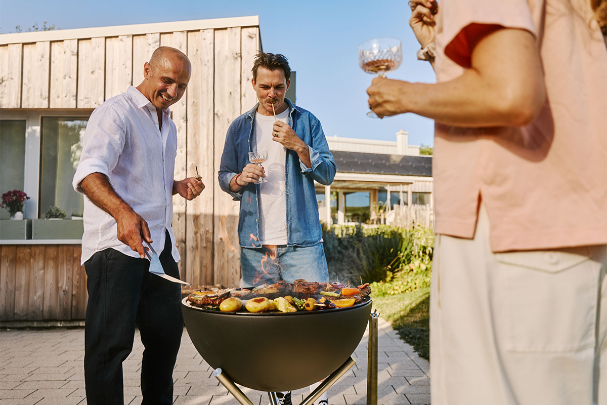 BOWL 57 Plancha BBQ Set low The 00256 Bowl 57 Plancha integrates seamlessly into the setting, where a person is cooking meat on a grill.