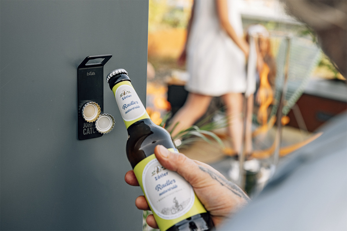 A person holding a bottle of beer near a door, enriched by the presence of the 00841 Johnny Catch Magnet Black Bottleopener, which merges design with utility.