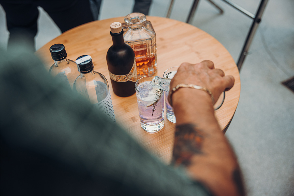 The 00570 Bowl 70 Board is shown as a person sitting at a table with a bottle of alcohol, creating a stylish and accessible visual.