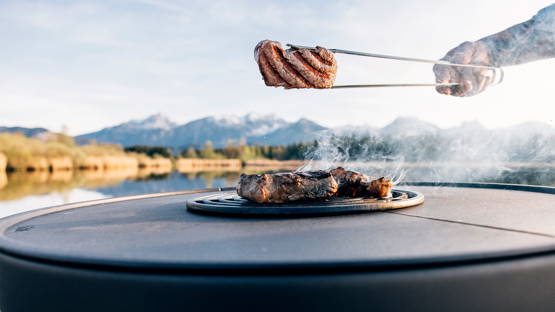 The photo presents a person is grilling meat on a grill, with the BOWL 70 Sear Grate.