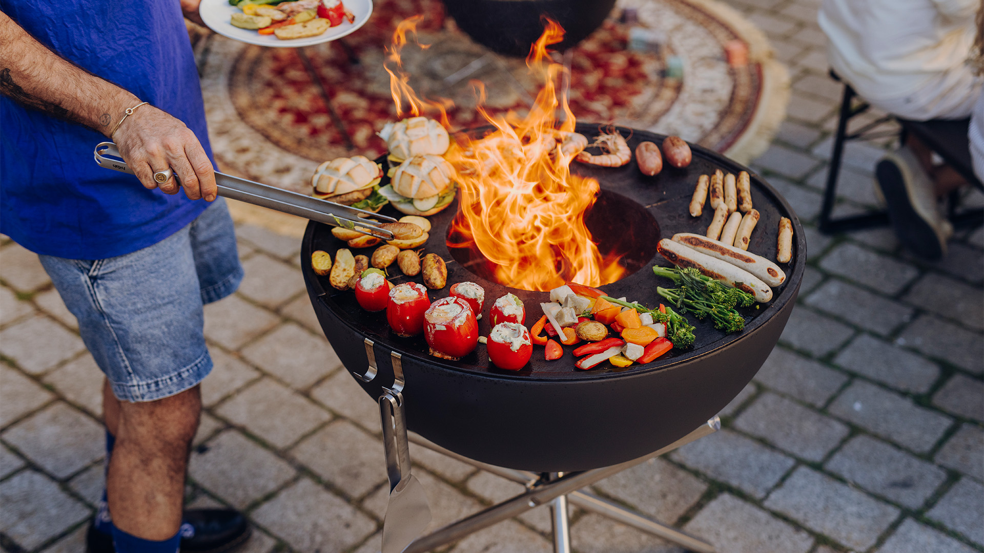 Scene showing a man is cooking food on a grill, where the Bowl 70 BBQ Set high stands out for its practical elegance.