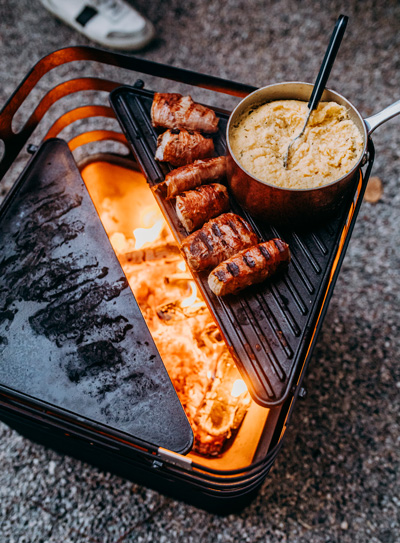 The photo presents a grill with meat and sauce on it, with the CUBE Fire basket black.