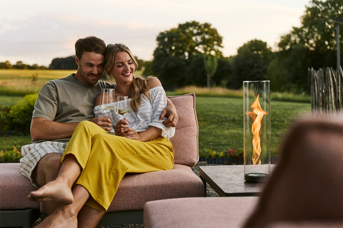 SPIN air 900 Built-in Ein Paar sitzt zusammen auf Gartencouch und schaut in die Flamme von SPIN air Einbau im Beistelltisch.