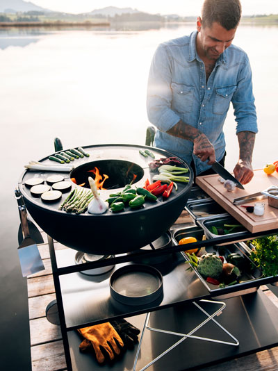 The BOWL FIRE KITCHEN is shown as a man cooking on a grill on a dock, creating a stylish and accessible visual.