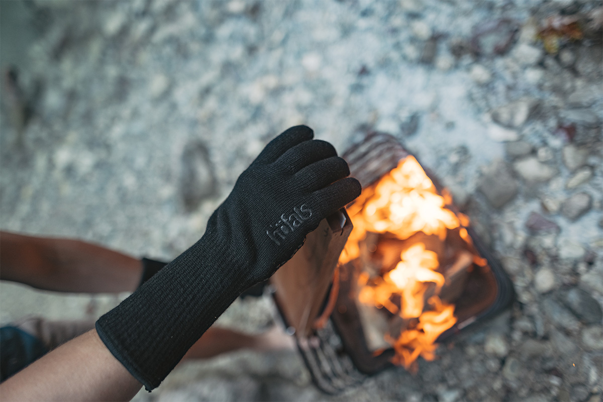 The 00715 Feuerhandschuhe Aramid integrates seamlessly into the setting, where a person holding grill accessoires over a fire