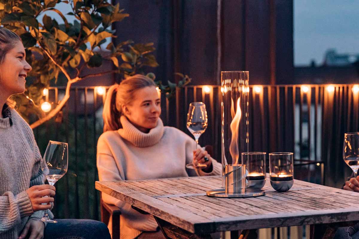 SPIN 90 Tabletop Fireplace silver Scene showing a family enjoying a meal together at a table outside at night, where the Spin 90 Tablefire silver stands out for its practical elegance.