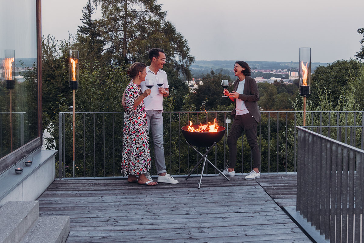 An image showing a man and woman standing on a deck with a fire, with the BOWL 57 Fire Set flex.