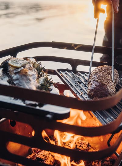 An inviting scene with a person grilling steaks on a grill, highlighted by the presence of the Cube Firebasket
