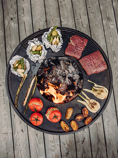 Illustrated is a grill with meat and vegetables on it, with the CUBE Plancha.