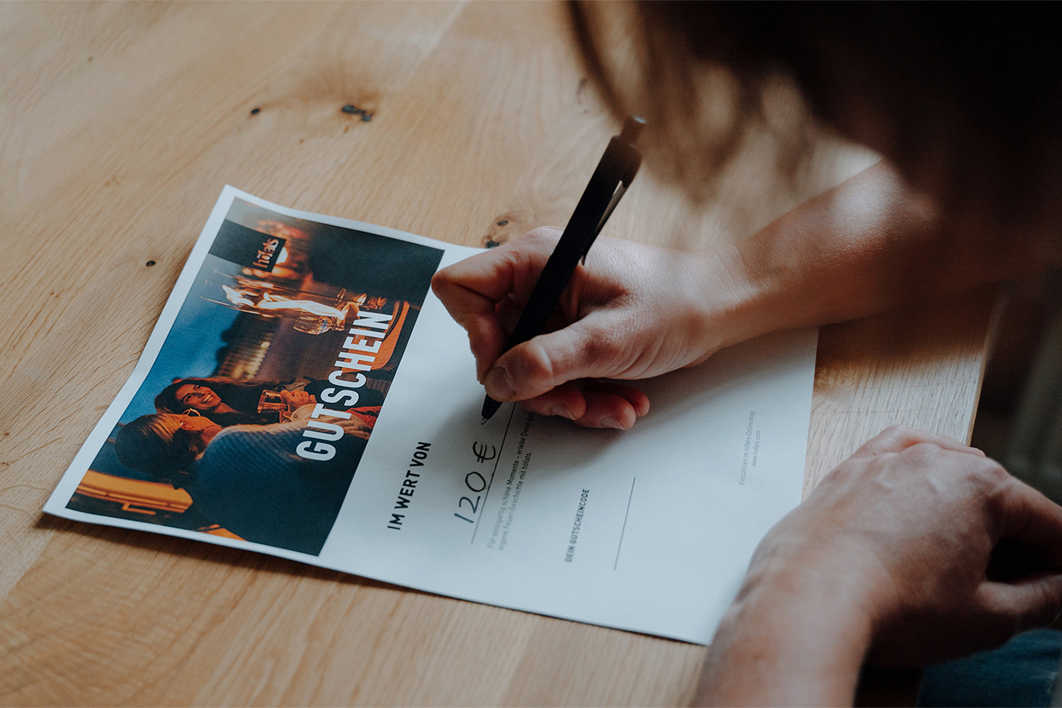 An image showing a person writing on a piece of paper, with the GIFT VOUCHER digital.