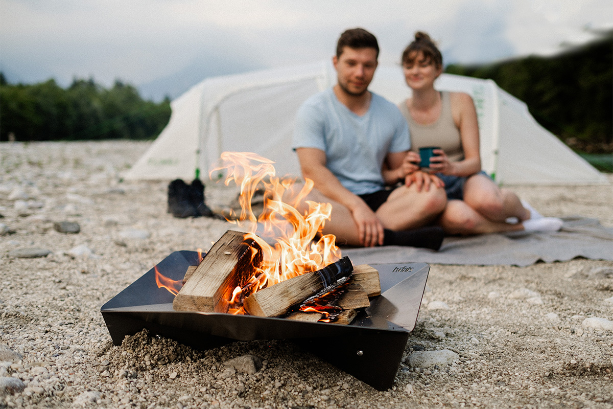 Experience a man and woman sitting next to a campfire with the refined touch of the Triple 65 Fireplace