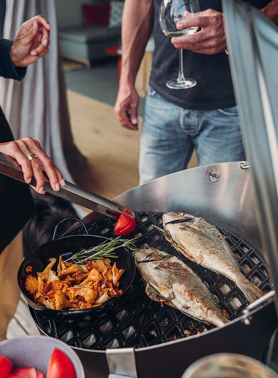 The 010301 CONE Cast Iron Grid is shown as a man cooking fish in a pan with vegetables, creating a stylish and accessible visual.