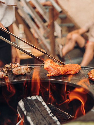 An image showing a man cooking food on a grill, with the FIRE TONGS.