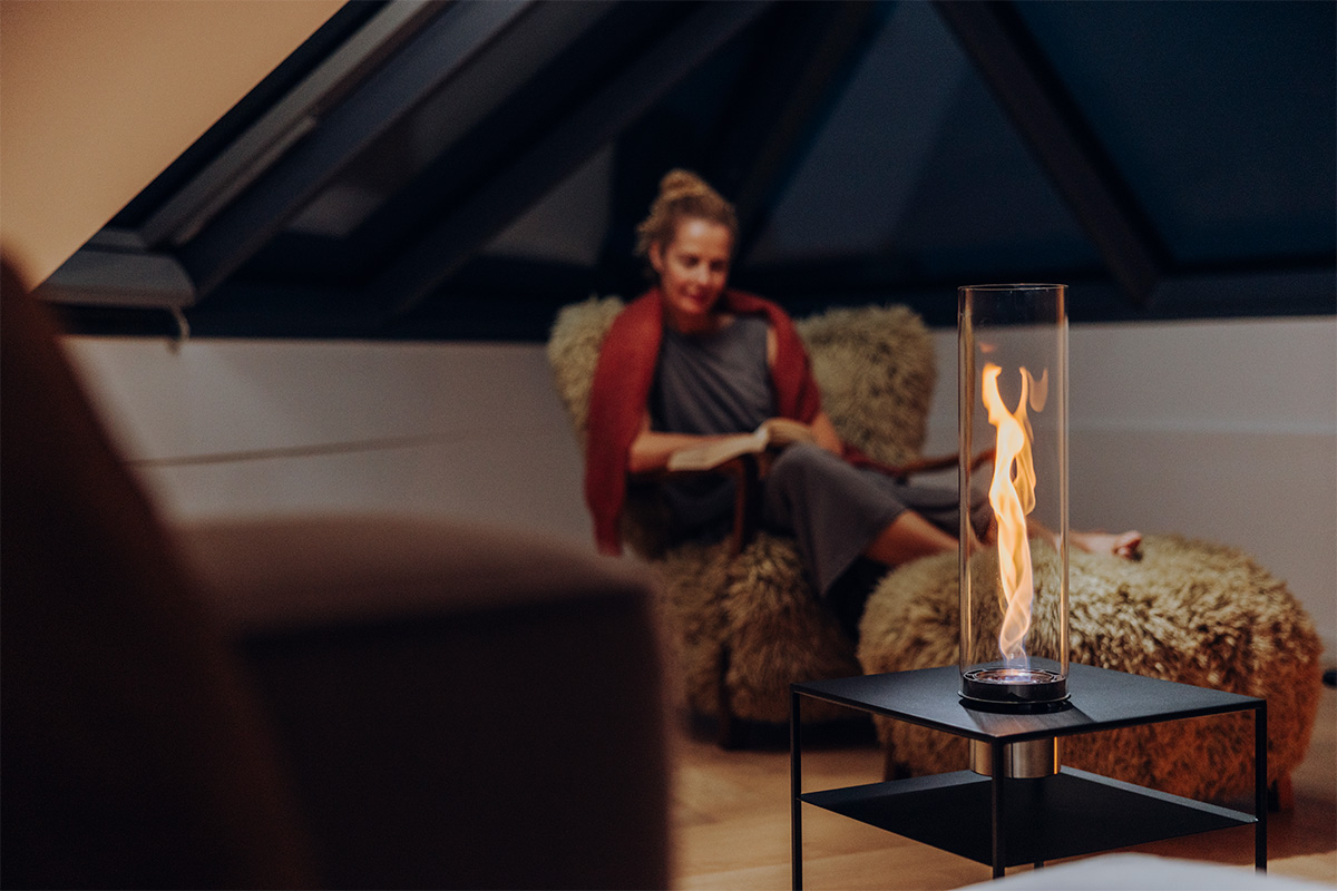 FIRE FRAME Lounge Table with SPIN air 1200 Built-in Eine Frau sitzt auf einem flauschigen Sessel und blickt in die Flamme von SPIN air 1200 Einbau, eingebaut in den FIRE FRAME Lounge-Tisch.