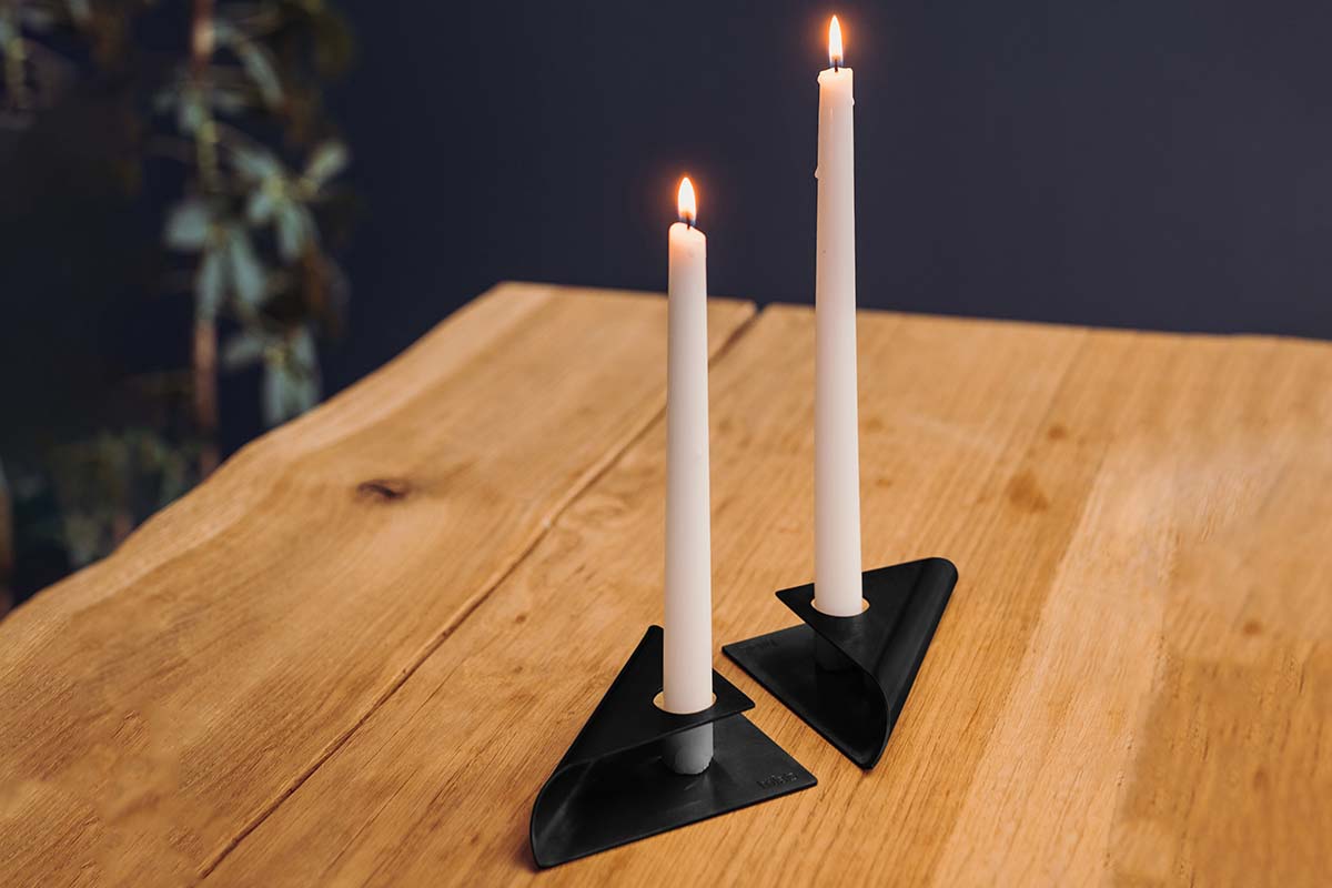 SQUARE CANDLE Candleholder black This image shows a pair of candles on a wooden table, with the SQUARE CANDLE Candleholder black.