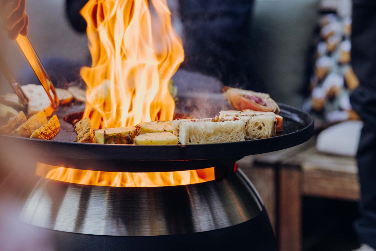 Grilling becomes an experience with the Moon 45 Plancha bbq set low, as the scene shows a dish being prepared outside.