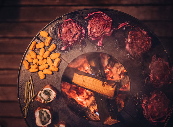 This image shows a grill with meat and vegetables on it, with the BOWL Fire Bowl.