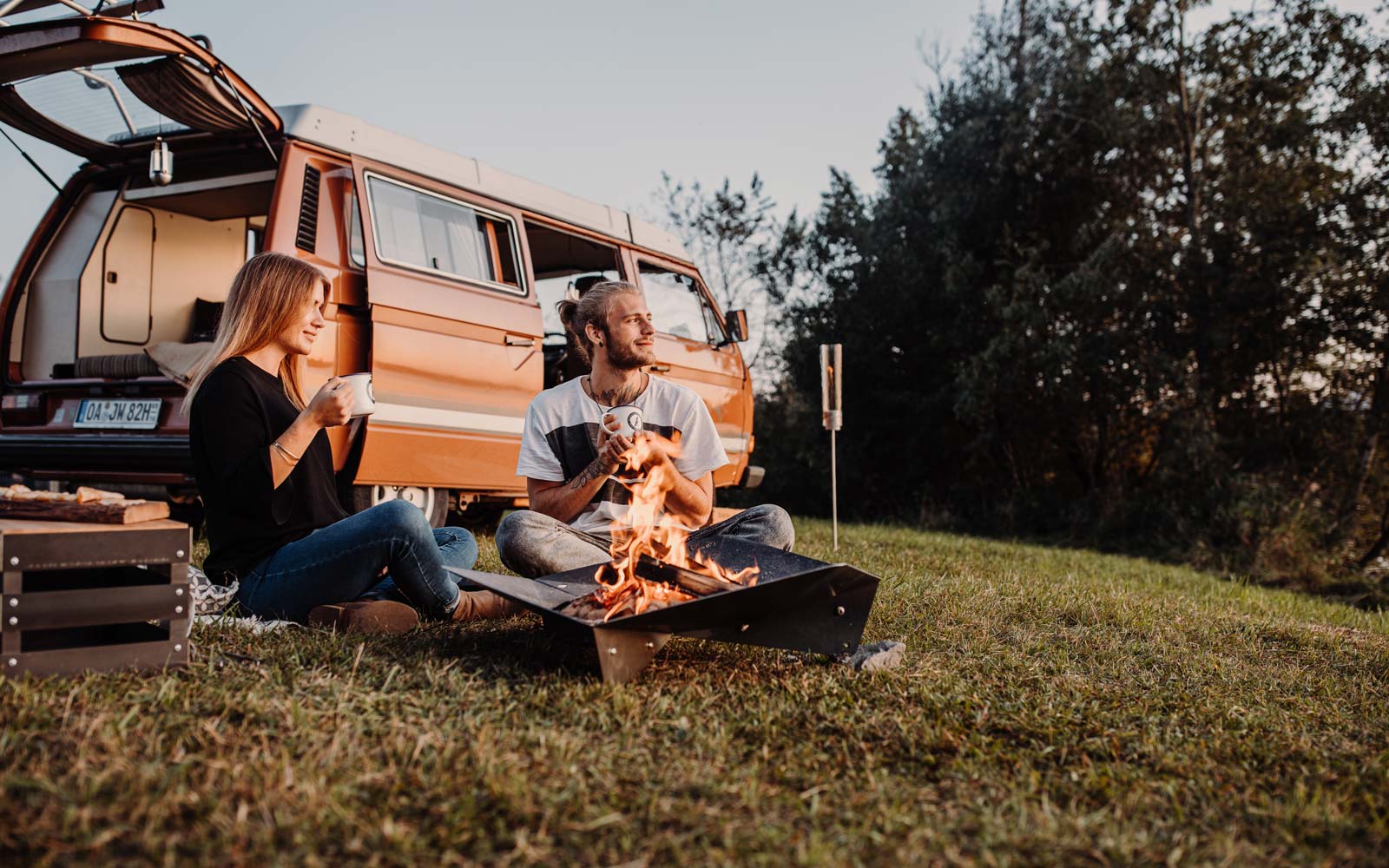 The Triple Fireplace is shown as a couple sitting on the grass next to a camper van, creating a stylish and accessible visual.