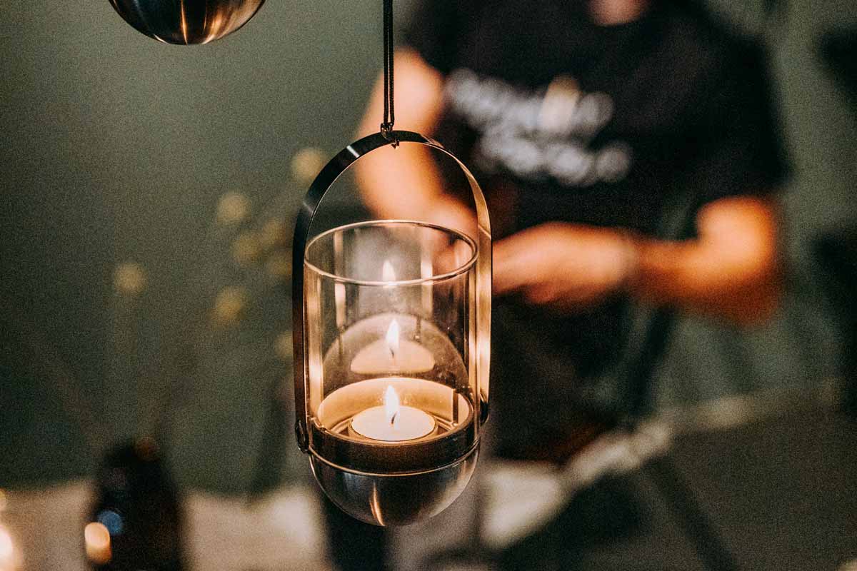 GRAVITY CANDLE Hanging System The Gravity Candle Hanging System integrates seamlessly into the setting, where a man is standing behind a table with a candle.