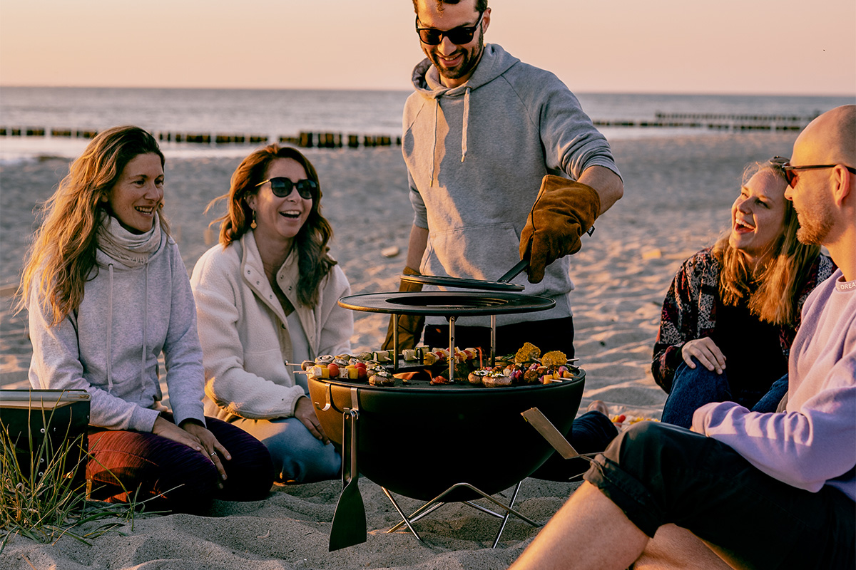 Illustrated is a group of people sitting on the beach, with the BOWL 57 Warming Ring.