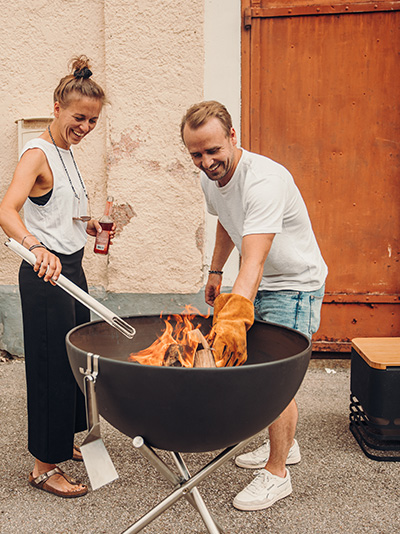A man and woman cooking on a grill, enriched by the presence of the Firegloves, which merges design with utility.
