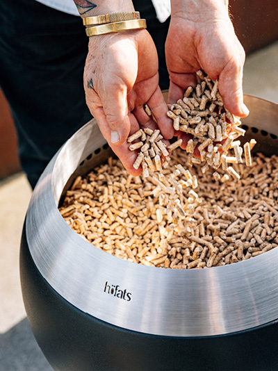 A person is putting wooden chips into a fire basket. Showing how to light the MOON 45