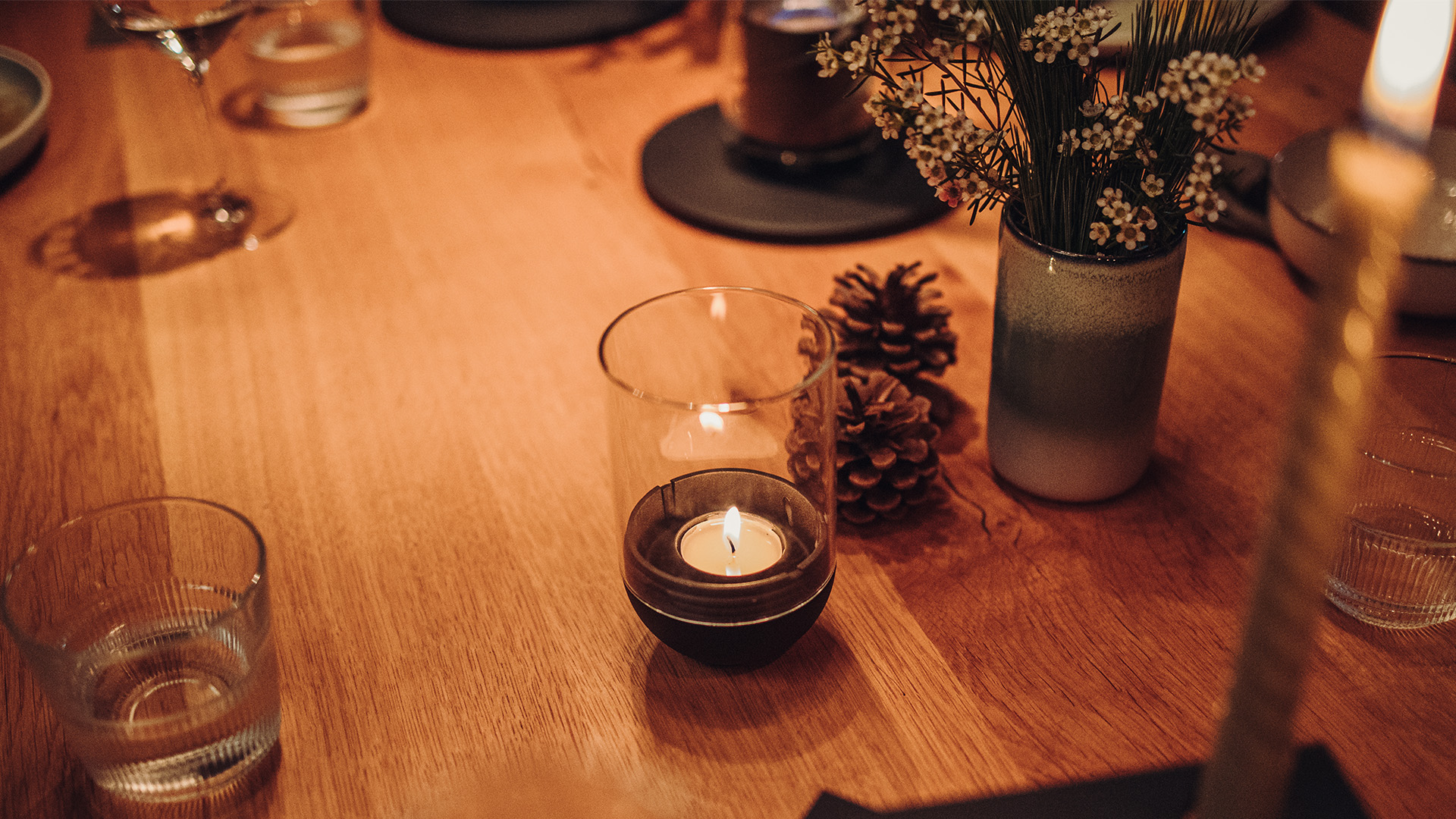 A table with a vase of flowers and candles, with the 00544 Gravity Candle black adding a functional and elegant touch to the scene.