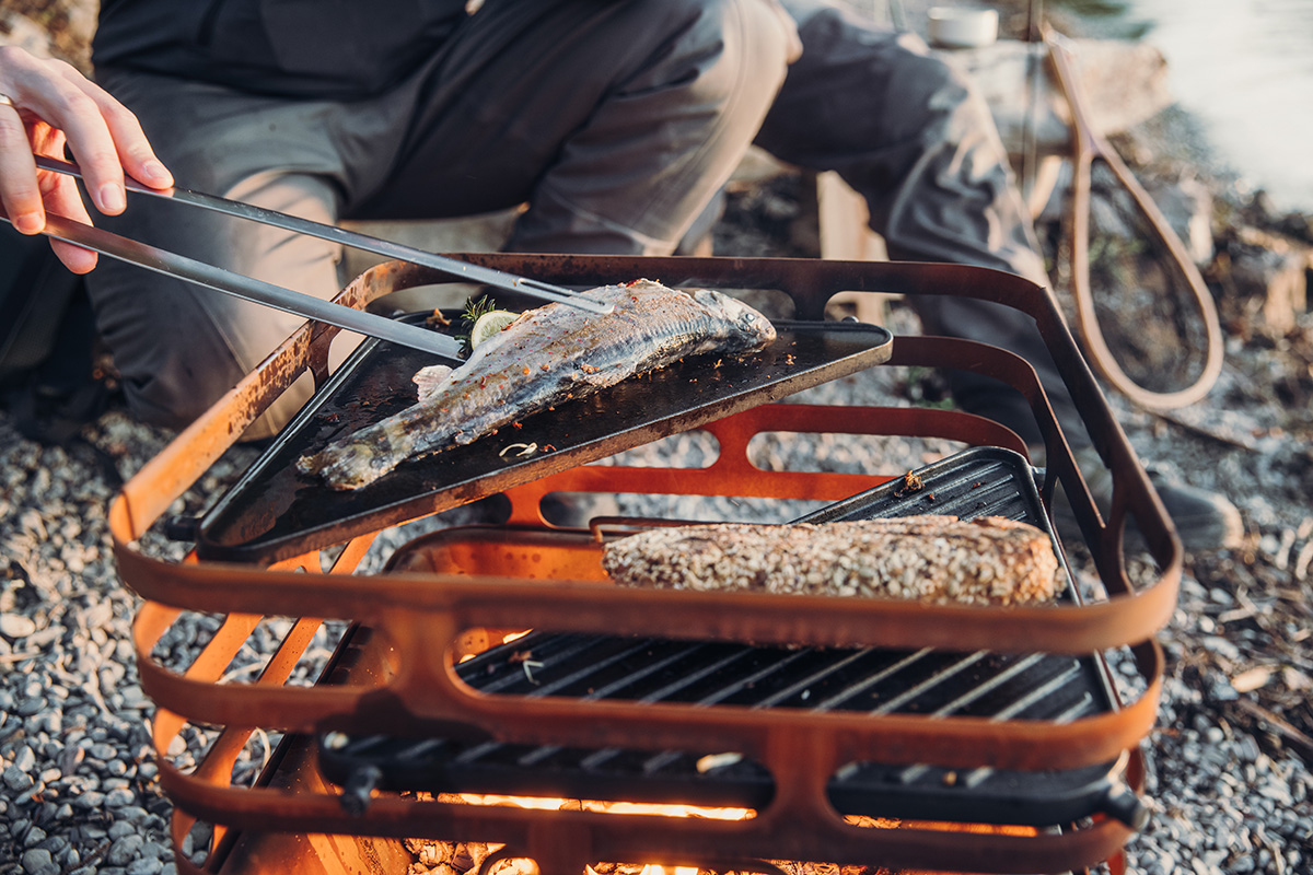 The photo presents a person is cooking food on a grill, with the CUBE Plancha.