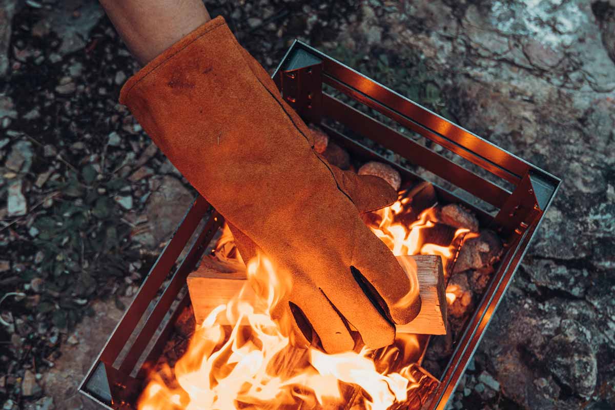 Fire Gloves Leather An image showing a person ' s hand holding a fire in a metal box