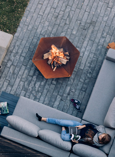 A woman laying on a couch next to a fireplace, with the Triple Fireplace adding a functional and elegant touch to the scene.