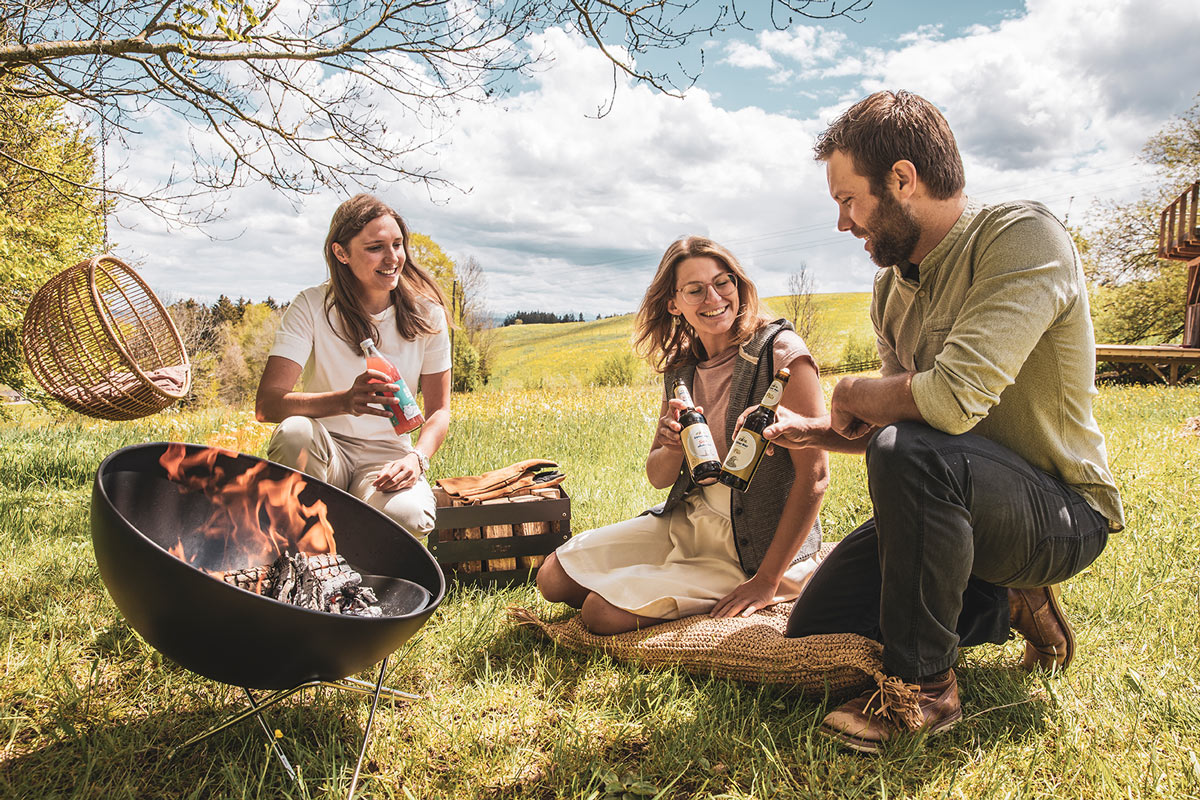 A view of a man and woman sitting on the grass, with the BOWL 57 Fire Set flex.