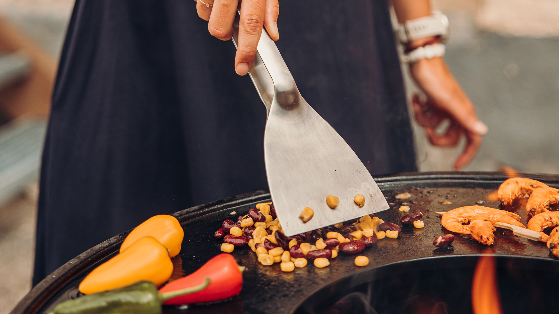 The photo presents a person is cooking food on a grill, with the Scraper.