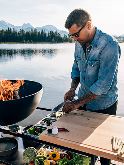 This image shows a man cooking on a grill, with the FIRE KITCHEN.
