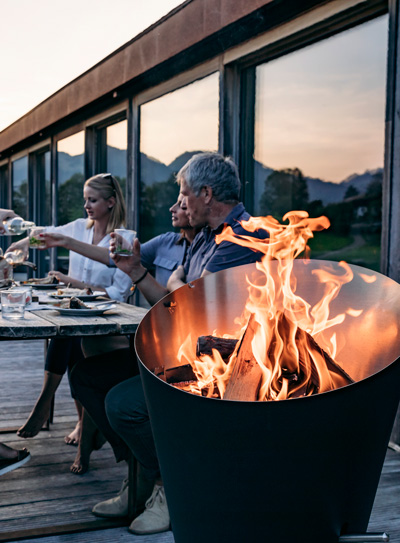 A depiction of a group of people sitting around a fire pit, featuring the Cone Charcoal Grill as a central and purposeful element.