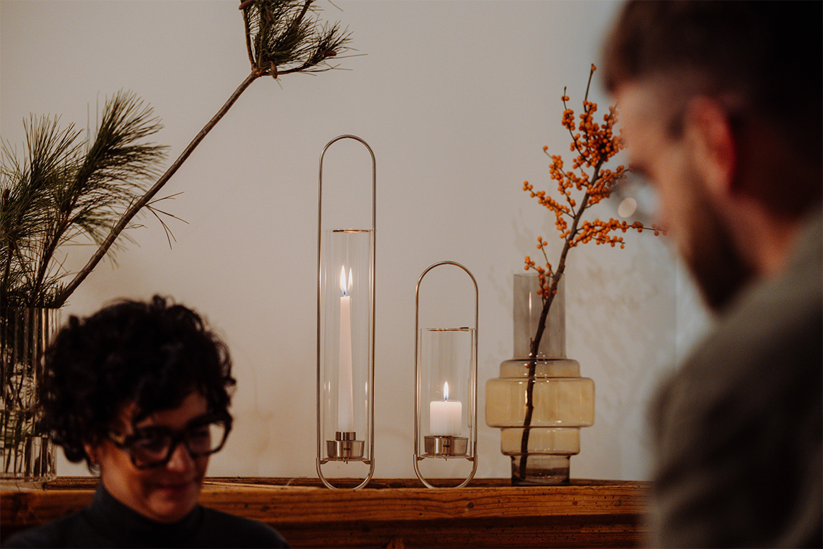 A depiction of a man sitting in front of a table with a vase and a candle, featuring the 00271 Oval Candle 55 as a central and purposeful element.
