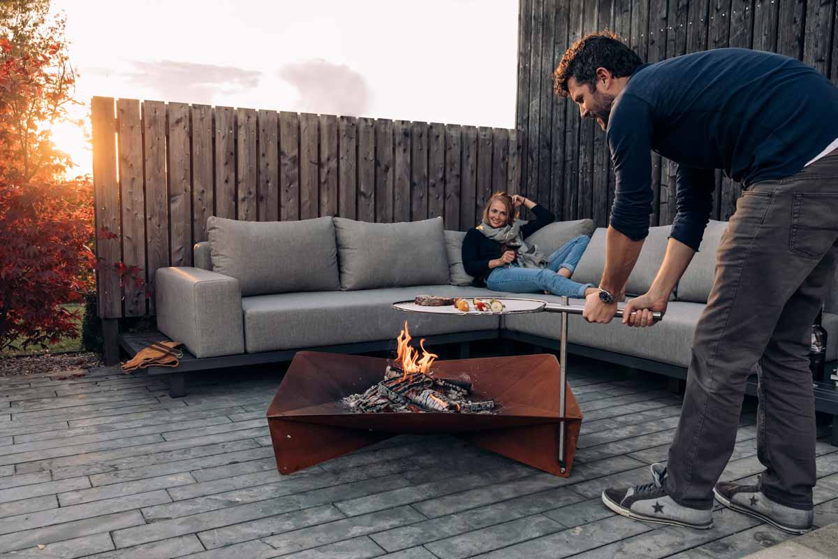 TRIPLE Grid 55 The Triple Grid 55 integrates seamlessly into the setting, where a man and woman are setting up a fire pit.