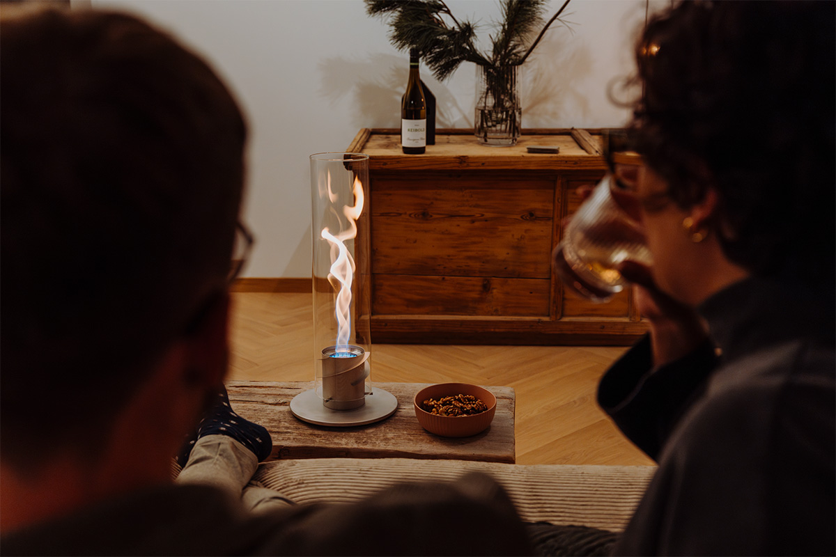SPIN 1200 Tabletop Fireplace grey The 00697 Spin 1200 Tablefire grey is shown as a man sitting on a couch with a candle on his lap, creating a stylish and accessible visual.