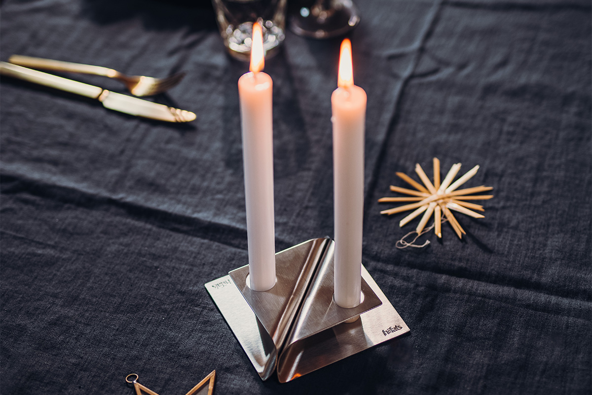 An image showing a candle and a napkin on a table, with the SQUARE CANDLE Candleholder silver.