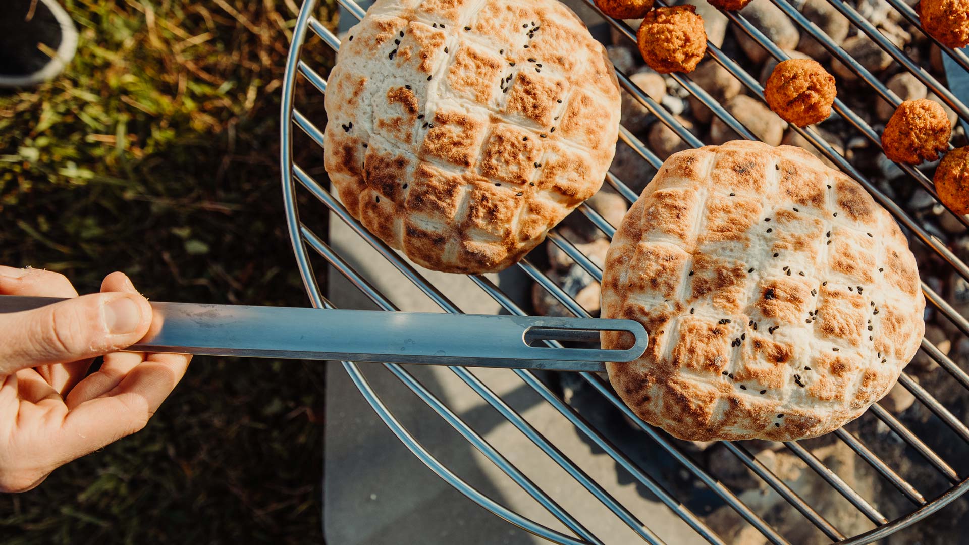 A depiction of a person is cooking some food on a grill, featuring the Triple 65 Fireplace BBQ Set as a central and purposeful element.