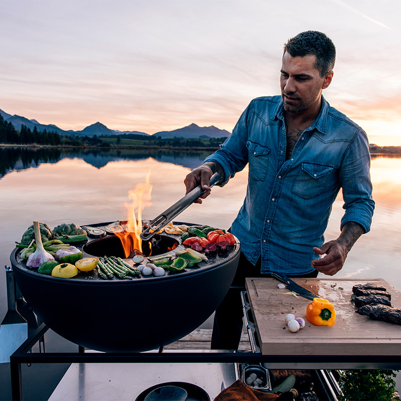 Depicted here is a man cooking on a grill, with the FIRE KITCHEN.