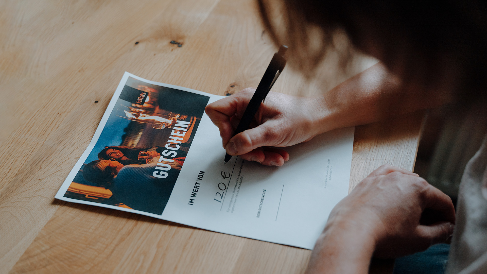 This image shows a person writing on a piece of paper, with the GIFT VOUCHER digital.