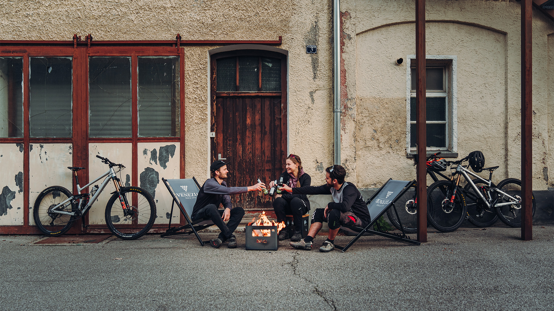 A couple of people sitting around a fire, enriched by the presence of the Beer Box Firebasket, which merges design with utility.