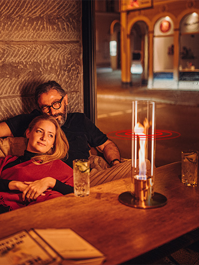 The photo presents a man and woman sitting on a couch, with the LOGO SPIN Table-top fireplace.