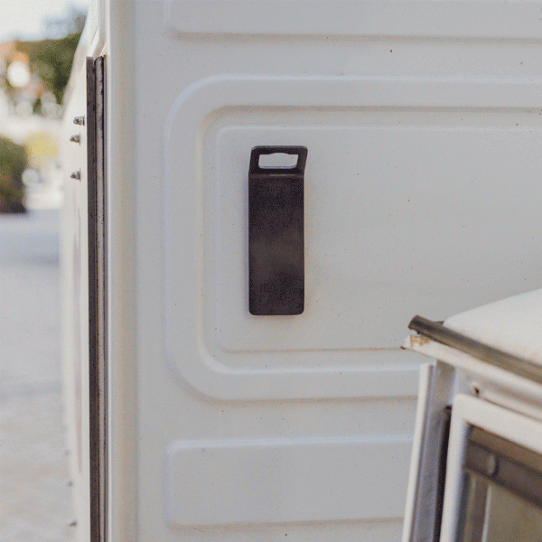 An animated picture of the 00841 Johnny Catch Magnet Black Bottleopener in action. A man opening his beverage in a sunny scene