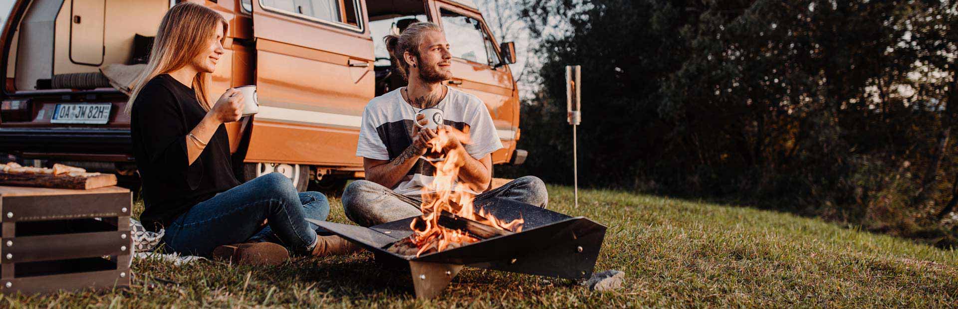 a couple sitting by a camper van on the grass.