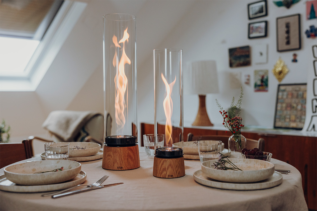 SPIN air 900 Tabletop fireplace oak SPIN air 1200 und 900 Tischfeuer Eiche natür stehen auf einem runden gedeckten Tisch im Hintergrund sind Bilder an der Wand